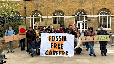 Crowd of students outside UCL building hold up handmade signs and giant banner reading Fossil Free Careers